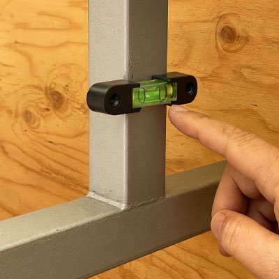 Main utilisant niveau à bulle magnétique noir vert pour vérifier alignement meuble bois - installation précise