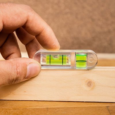 Main tenant niveau à bulle transparent avec 3 fioles vertes sur planche bois - outil mesure compact précision
