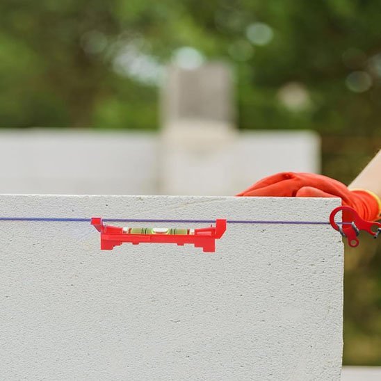Niveau à bulle rouge fixé sur un muret blanc en extérieur avec gants de travail orange