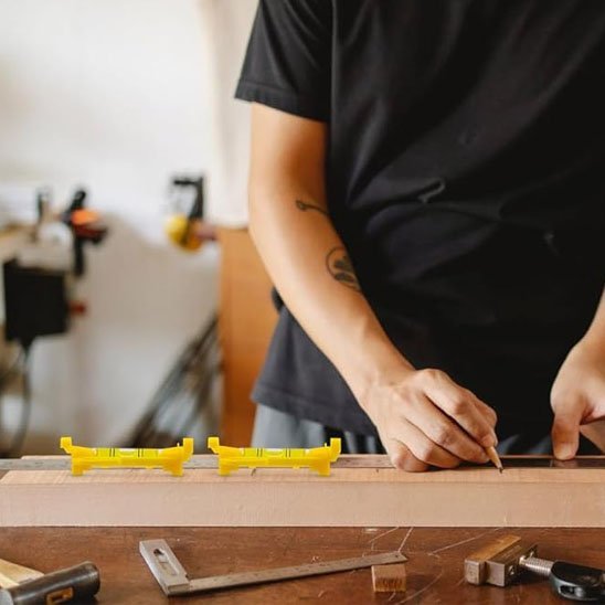 Artisan utilisant des niveaux à bulle jaunes sur une planche de bois dans un atelier