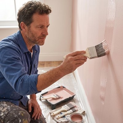 Homme peignant un mur rose avec un pinceau professionnel - finition lisse et précise