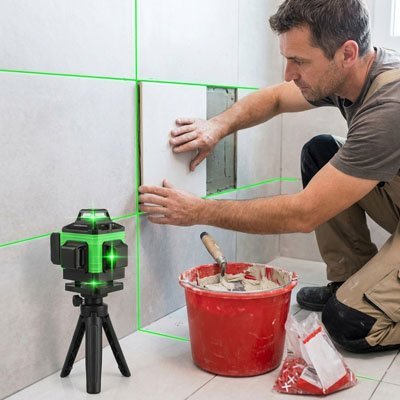 Homme installant carrelage avec niveau laser): "Carreleur installant carreaux muraux avec niveau laser 360° vert - alignement parfait travaux rénovation