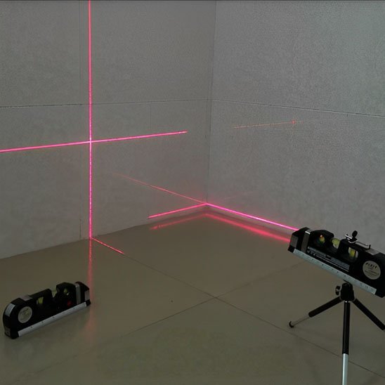 Niveau laser avec trépied projetant lignes horizontales et verticales rouges sur mur - démonstration en intérieur"