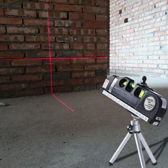 Niveau laser professionnel sur trépied en action sur chantier - projection de lignes de référence sur mur de briques