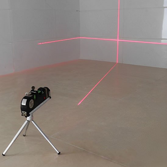Niveau laser avec trépied projetant croix de nivellement rouge dans angle de pièce vide