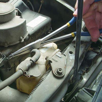 Pince à bec extra-longue manipulant un tuyau dans un moteur de voiture ancien