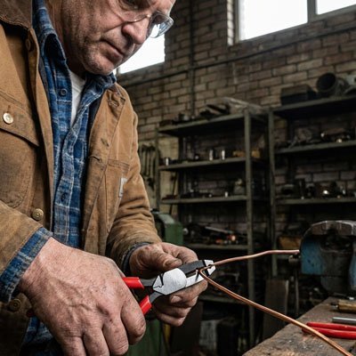  Ouvrier coupant du fil électrique avec une pince coupante professionnelle à mâchoires acier dans un atelier industriel