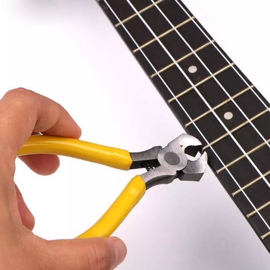 Pince coupante ergonomique à poignées jaunes coupant une corde de guitare sur manche - outil de précision pour luthier