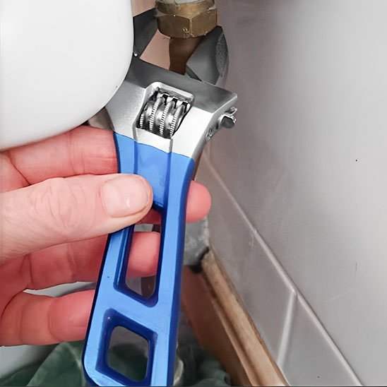 Clé à molette bleue utilisée sur un raccord de plomberie