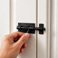 Main actionnant un loquet porte noir sur une porte blanche