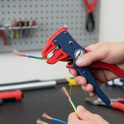 Pince à dénuder rouge et bleue dénudant un câble tricolore sur un établi d'atelier