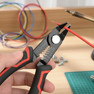 Pince à dénuder rouge et noire dénudant un câble rouge sur un établi d'atelier – Bricolage JP
