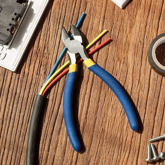 Pince coupante dénudant des fils électriques multicolores sur surface en bois