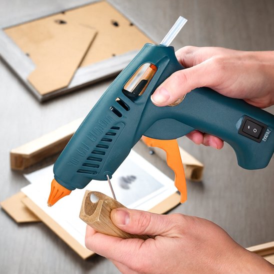 Mains tenant un pistolet à colle thermofusible pour assembler un cadre en bois