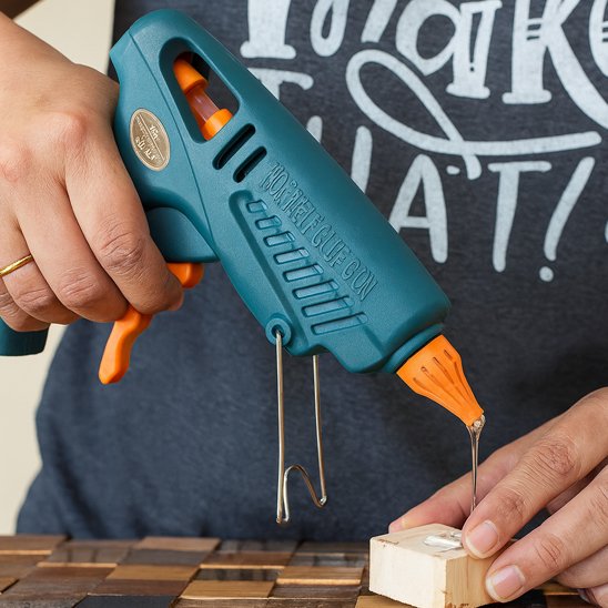 Pistolet à colle thermofusible bleu et orange en action sur un projet de bricolage