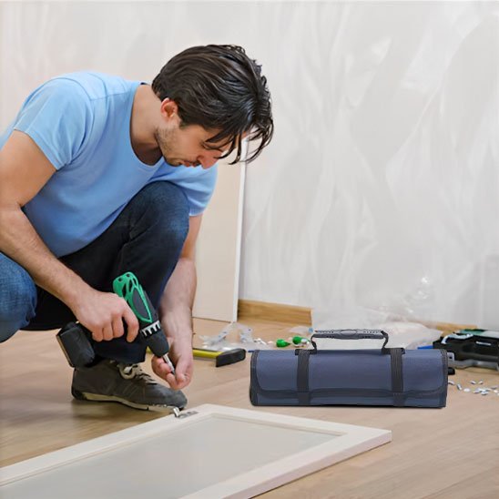 Artisan en t-shirt bleu utilisant une perceuse verte avec un sac à outils enroulable Bleu posé à côté sur un chantier